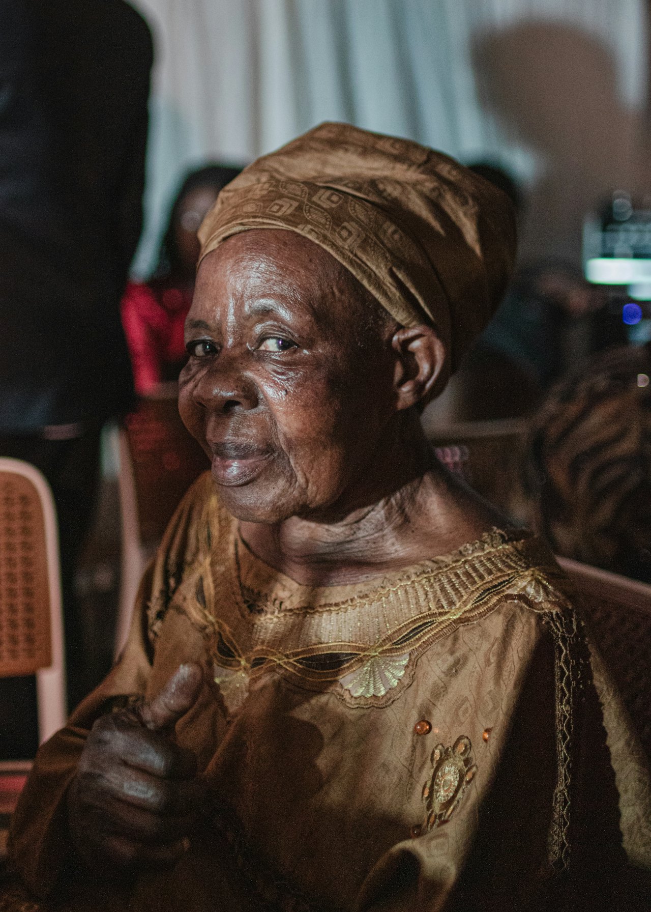 An elderly woman in a headwrap giving a thumbs up