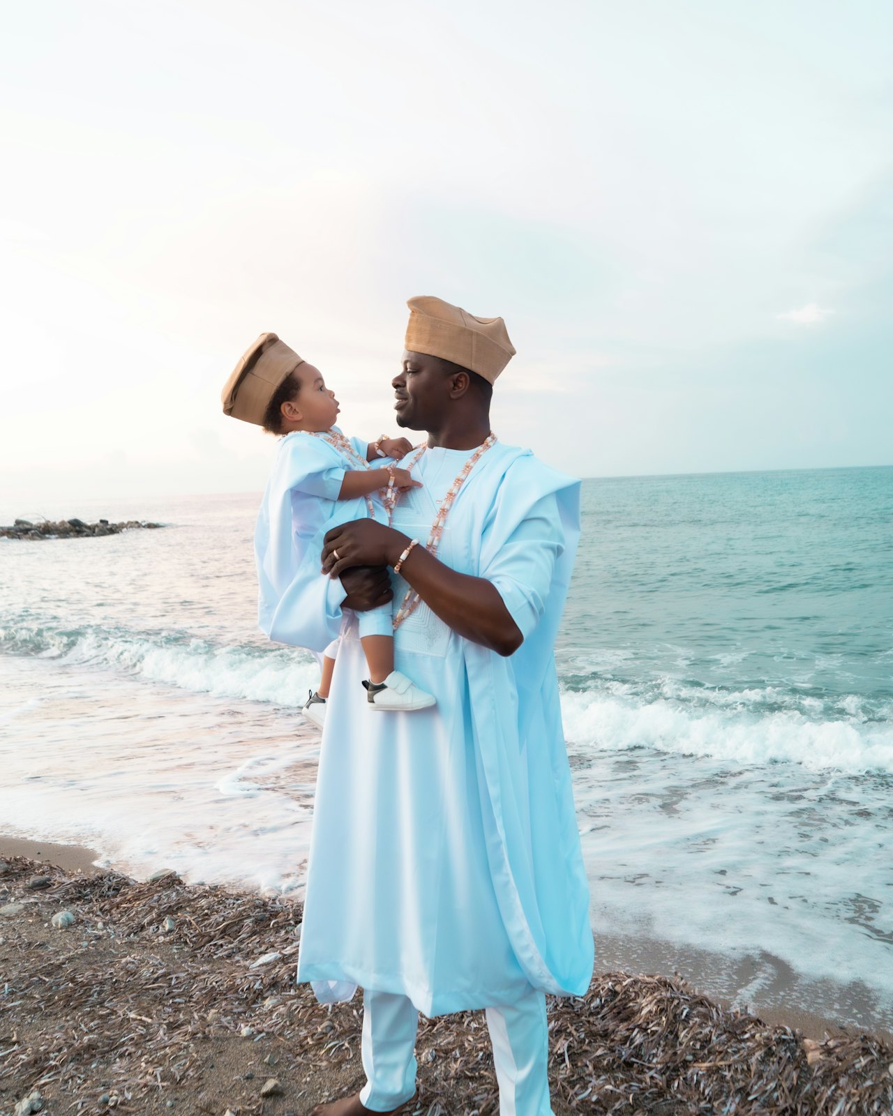 A father in traditional dress holding his baby by the sea