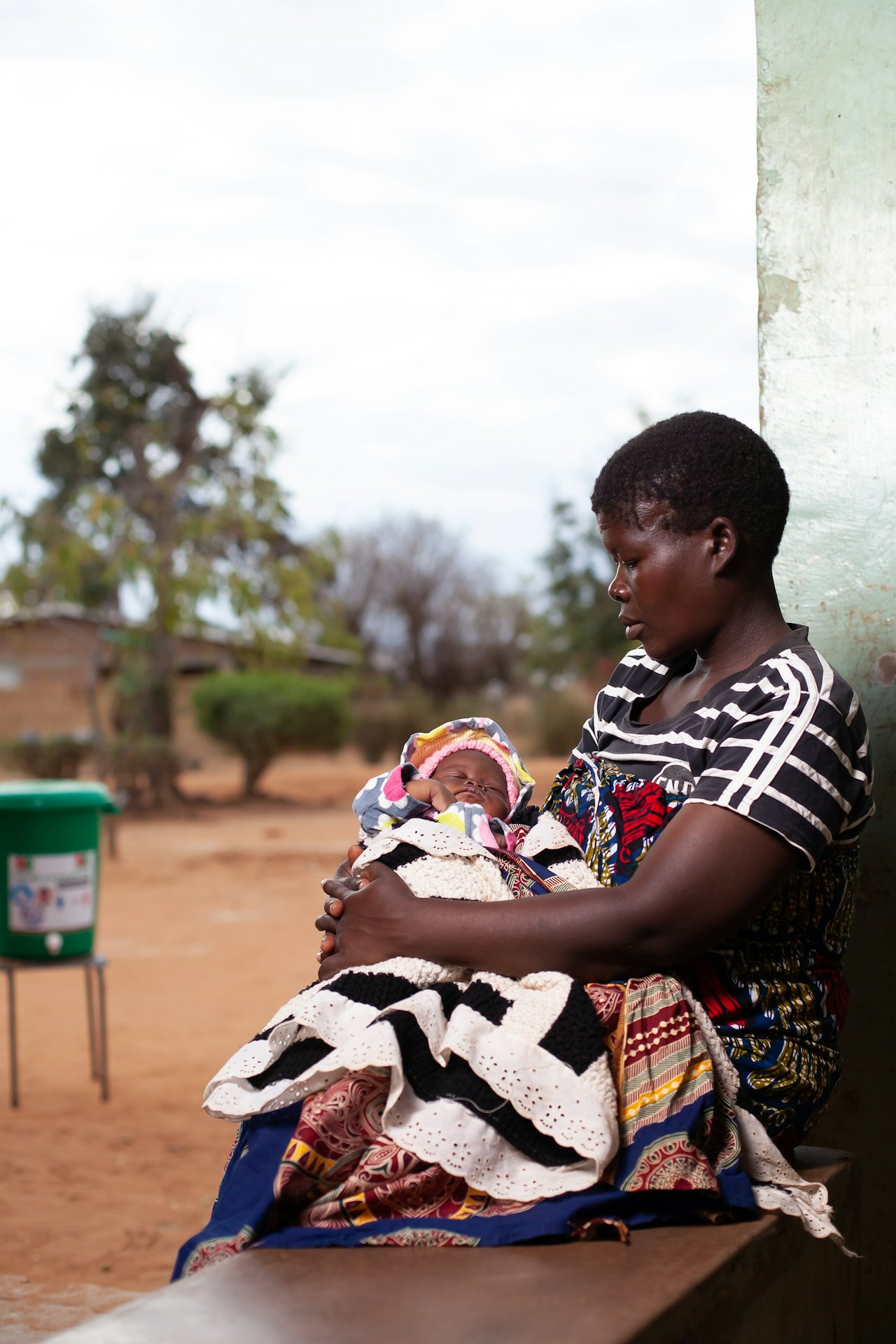A mother holding her baby outdoors beside a health centre